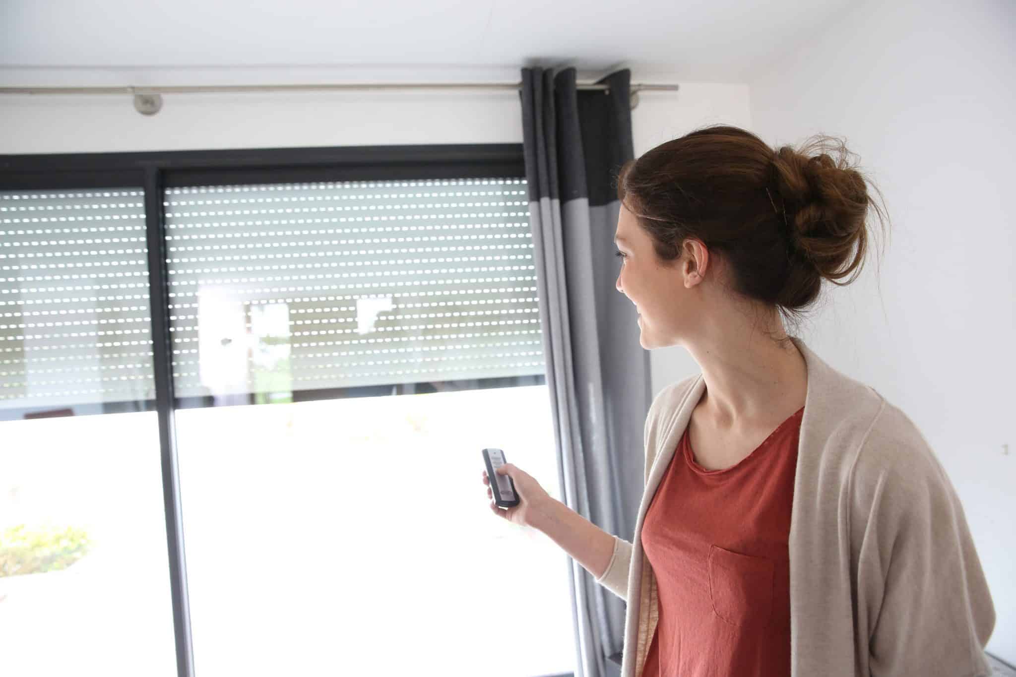 Frau benutzt eine Fernbedienung, um Fensterjalousien zu verstellen.