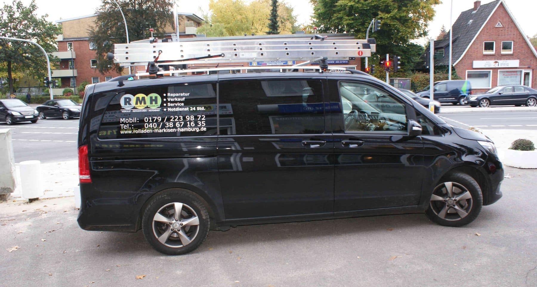 Ein schwarzer Lieferwagen mit Firmenlogo und einer darauf montierten Leiter steht am Straßenrand.
