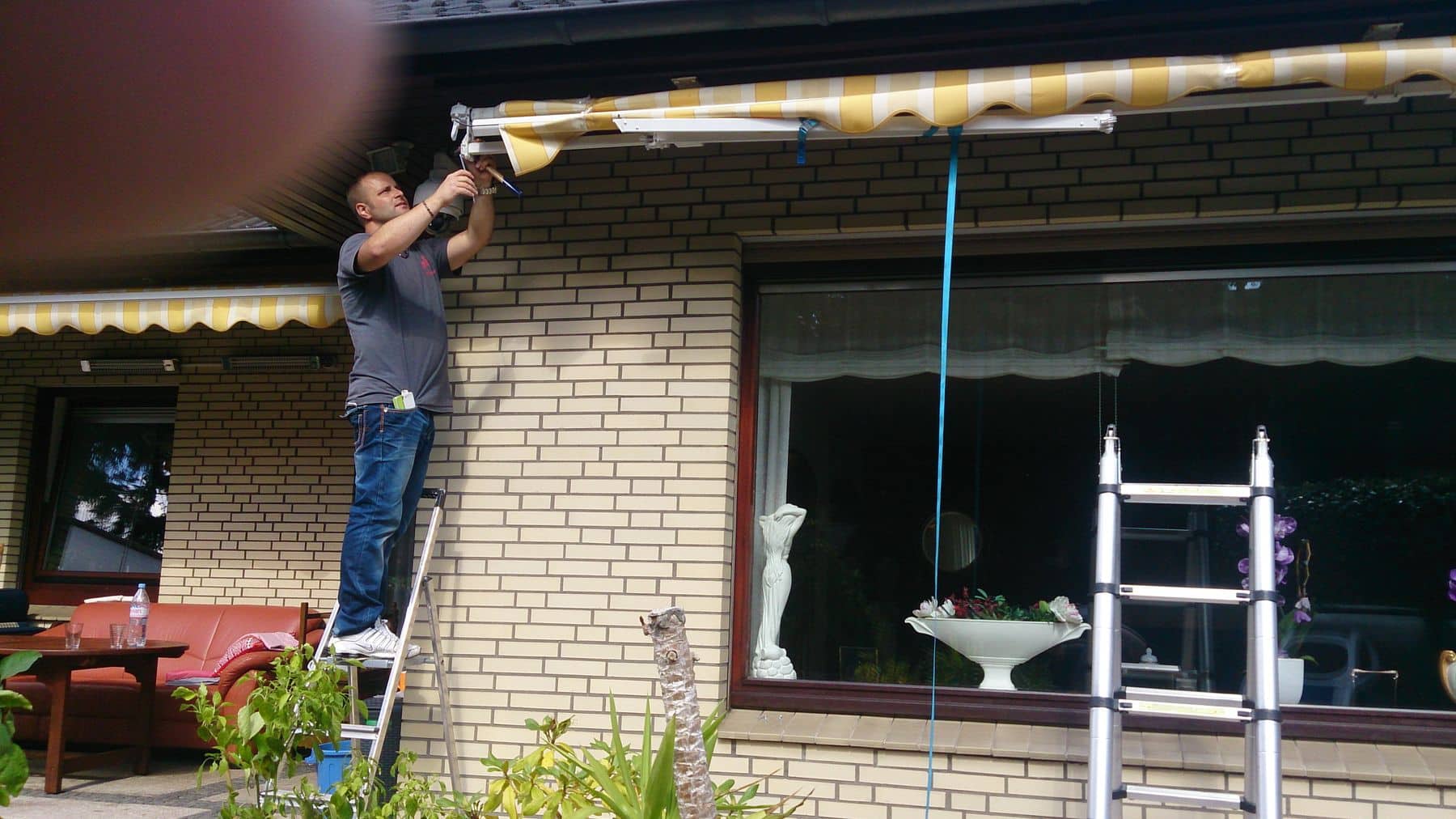 Mann repariert eine Markise vor einem Haus.