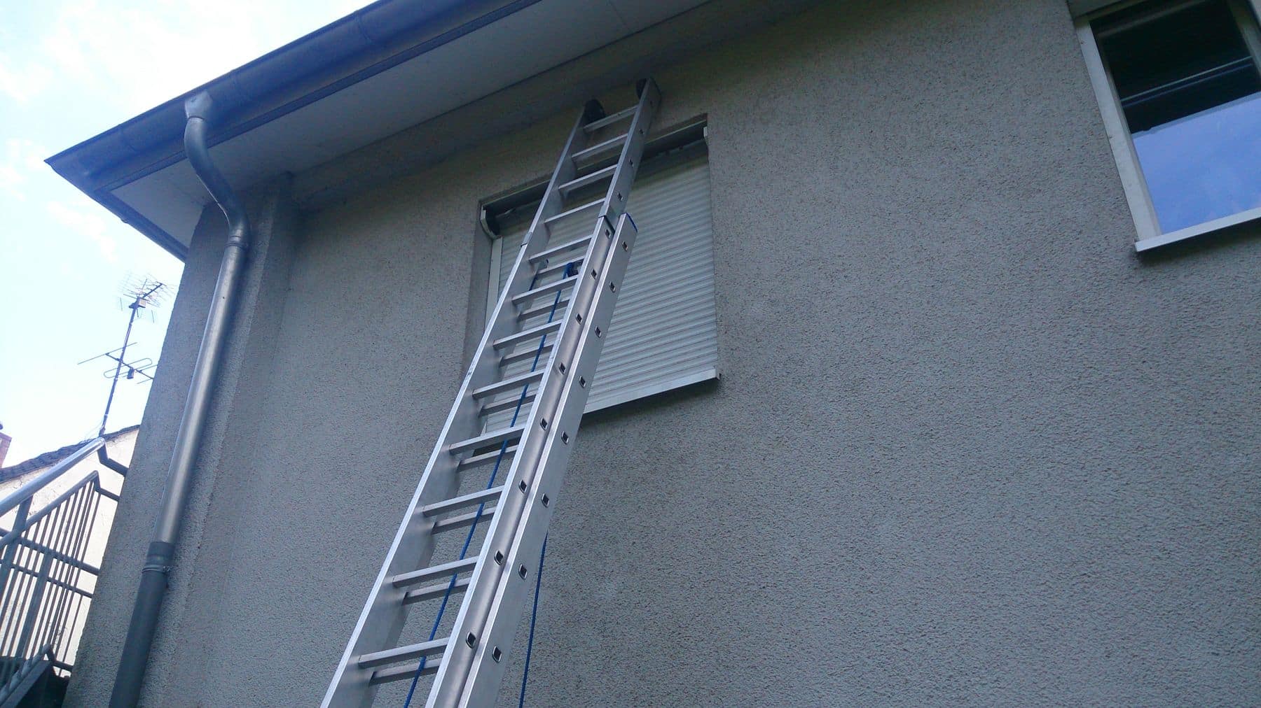 Eine an ein Gebäude gelehnte Leiter, die zu einem Fenster mit Fensterläden führt.